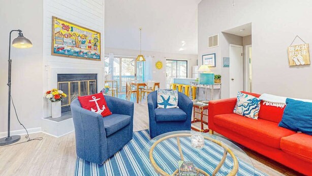 Ein Wohnzimmer mit Kamin, einem roten Sofa, blauen Sesseln, einem Couchtisch und einem Gemälde an der Wand.