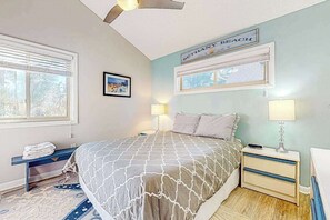 Un dormitorio con cama, mesitas de noche, ventana y ventilador de techo, además de un letrero en la pared.