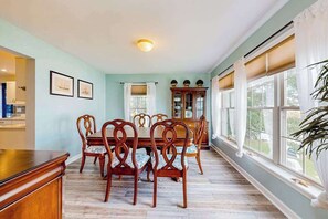 A dining room with a wooden table and chairs, a cabinet, and a window with curtains. - The Reservation - dog-friendly home with fenced yard, deck, grill, & beach gear (Ocean View)