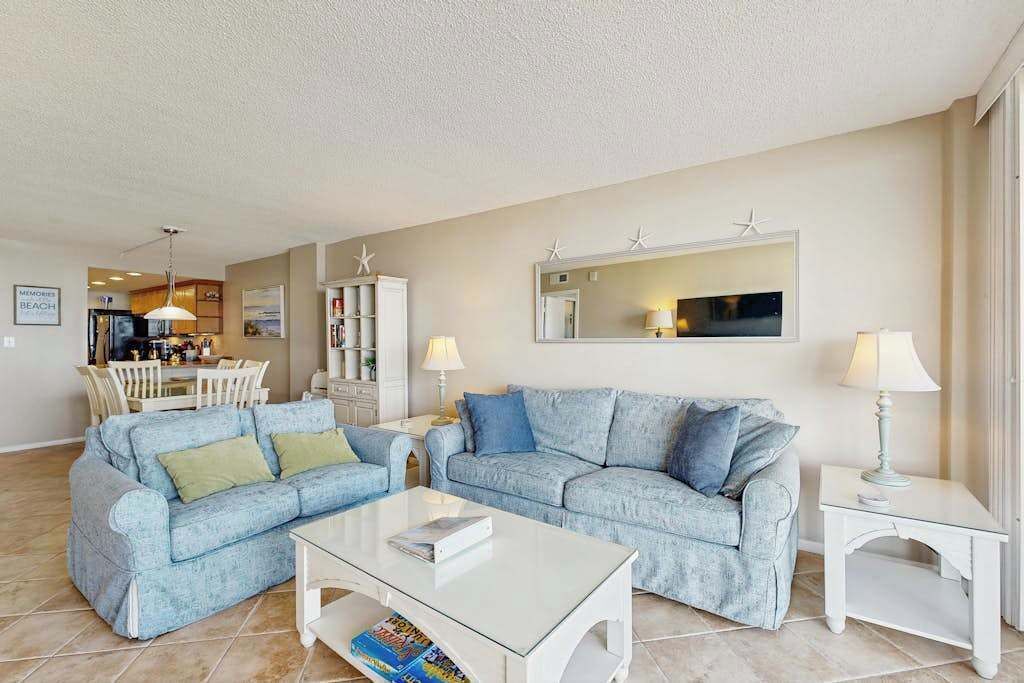 A living room with a sofa set, a coffee table, a dining area with chairs, and a kitchen in the background.