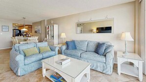 Un salon comprenant un ensemble de canapés, une table basse, un coin repas avec des chaises et, au fond, une cuisine.