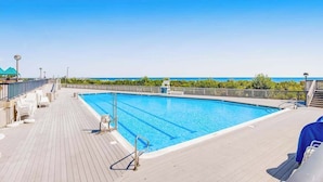 Une piscine à l’eau d’un bleu cristallin, entourée d’une terrasse en bois, et offrant une vue sur l’océan.