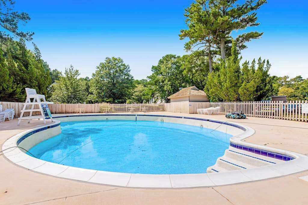 A swimming pool with a wooden deck, a small building, and a white picket fence.