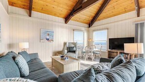 Una sala de estar acogedora con techo de madera, televisor, comedor con sillas y un ventanal grande.