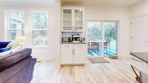 Eine moderne Küche mit weißen Schränken, einer Arbeitsplatte mit Kaffeemaschine und Blick auf den Garten durch Glastüren.