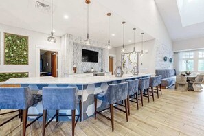 Una cocina moderna con una isla grande, taburetes de bar, luces colgantes y un televisor de pantalla plana.