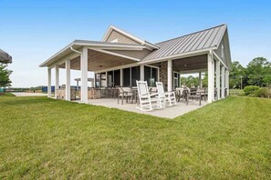 A covered outdoor patio with a stone fireplace, white chairs, and a dining table. - Millville By The Sea home w/3 pools, pickleball, fitness center, fireplace, dock (Millville)