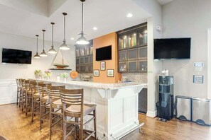 A kitchen with a central island, bar stools, pendant lights, a built-in oven, and a TV mounted on the wall. - Millville By The Sea home w/3 pools, pickleball, fitness center, fireplace, dock (Millville)
