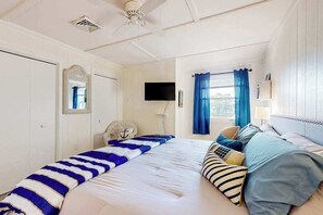 A bedroom with a bed, a television, a ceiling fan, a window with curtains, and a door.