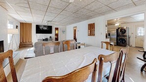 En matplats med ett stort bord, stolar, en takfläkt, en tv och ett köksområde med hushållsapparater.