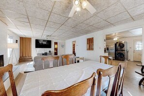A dining area with a large table, chairs, a ceiling fan, a television, and a kitchen area with appliances. - Town of Dewey Beach charming dog-friendly home with washer/dryer (Dewey Beach)