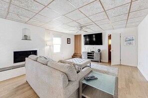 A living room with a sofa, a glass coffee table, a flat-screen TV, a fireplace, and a ceiling fan. - Town of Dewey Beach charming dog-friendly home with washer/dryer (Dewey Beach)