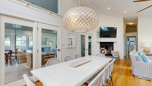 A spacious dining area with a long table and wicker chairs, a large decorative light fixture, and a television mounted on the wall. - Experience Classic Dewey Charm at This Coastal Retreat with Hot Tub (Dewey Beach)