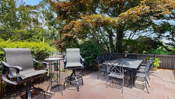 An outdoor patio with a table and chairs, surrounded by greenery and trees. - Experience Classic Dewey Charm at This Coastal Retreat with Hot Tub (Dewey Beach)