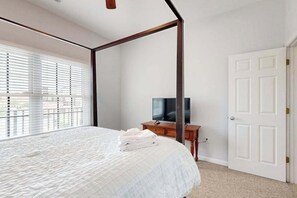 Ein Bett mit Baldachin, ein Fernseher auf einem Holzständer, eine weiße Tür und ein Fenster mit Jalousien.