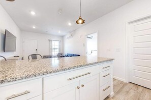 Cocina moderna con encimeras de granito, armarios blancos y una lámpara colgante.
