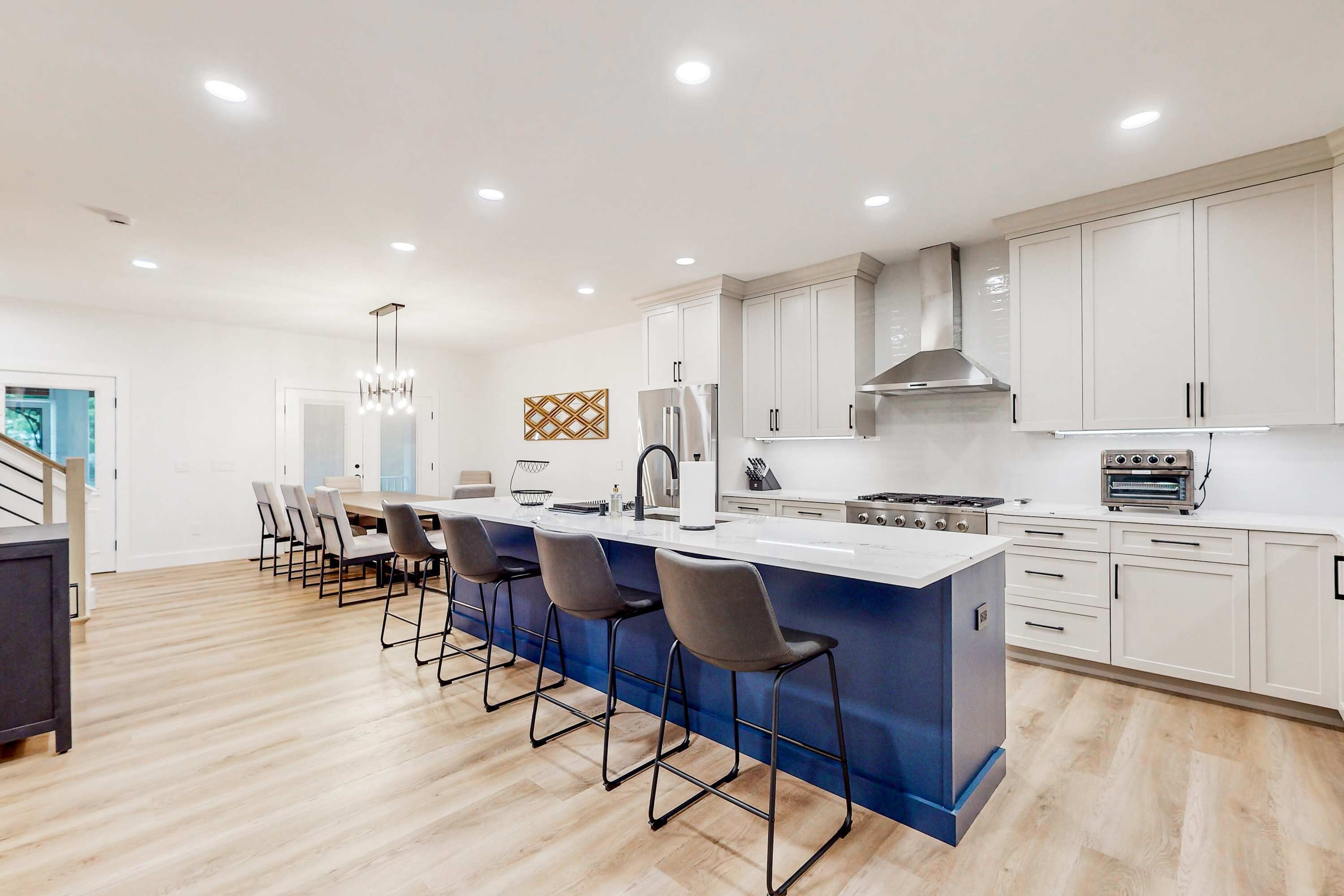 A modern kitchen with a central island, bar stools, and white cabinetry.