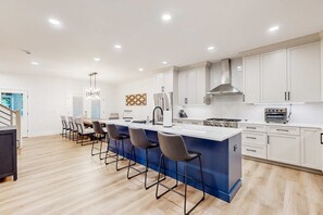 A modern kitchen with a central island, bar stools, and white cabinetry. - Stunning Peninsula getaway with pools, hot tubs, sports courts, & on-site golf (Millsboro)