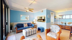 Un salon avec un mur bleu, un ventilateur de plafond, un canapé, un fauteuil et une petite table.