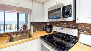 Une cuisine avec des meubles blancs, un four à micro-ondes en acier inoxydable, une cuisinière et une fenêtre donnant sur un balcon.