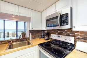 A kitchen with white cabinets, a stainless steel microwave, a stove, and a window overlooking a balcony. - Sea Colony 7th floor condo w/ free WiFi, shared tennis court - ocean view (Bethany Beach)