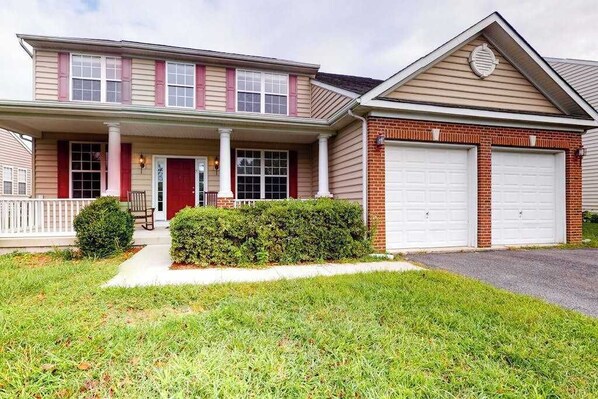 A two-story house with a front porch, a red door, and two garage doors. - Wedgefield house w/ free WiFi, gas grill, outside shower & community pool (Ocean View)