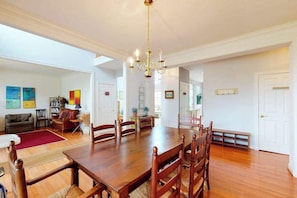 A dining area with a wooden table, chairs, and a chandelier. There are two doors and a bench in the background. - Wedgefield house w/ free WiFi, gas grill, outside shower & community pool (Ocean View)