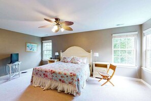 A bedroom with a bed, a ceiling fan, bedside tables, a chair, and windows. - Wedgefield house w/ free WiFi, gas grill, outside shower & community pool (Ocean View)