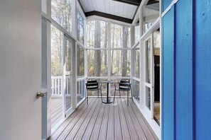 A covered deck with a table and chairs, large windows, and a view of trees. - Middlesex Beach house w/ outside shower, grill & community private beach (Bethany Beach)