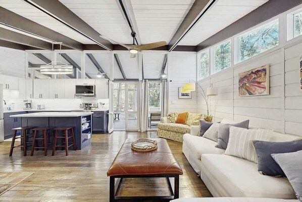 A spacious living area with a large sofa, a coffee table, and a kitchen area with a central island and bar stools. - Middlesex Beach house w/ outside shower, grill & community private beach (Bethany Beach)