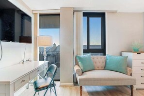 Ein modernes Wohnzimmer mit Sofa, Wand-Fernseher, Schreibtisch mit Stuhl und großem Fenster.