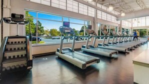 Ein Fitnessraum mit Laufbändern und Steiger, großen Fenstern und Blick auf den Parkplatz.