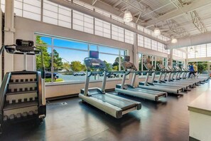 Ein Fitnessraum mit Laufbändern und Steiger, großen Fenstern und Blick auf den Parkplatz.