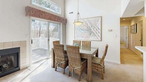 A dining area with wicker chairs, a glass table, a fireplace, and a large window. - Sea Colony Tennis condo with tennis court, pool, washer/dryer & covered porch (Bethany Beach)
