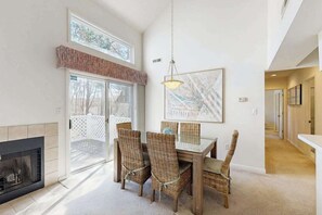En matplats med flätade stolar, ett glasbord, en öppen spis och ett stort fönster.