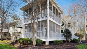 A two-story house with a balcony, surrounded by trees and a well-maintained lawn. - Sea Colony Tennis condo with tennis court, pool, washer/dryer & covered porch (Bethany Beach)