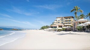 A beachfront hotel with multiple floors, outdoor seating, and palm trees. - Garza Blanca Preserve Resort & Spa (Puerto Vallarta)