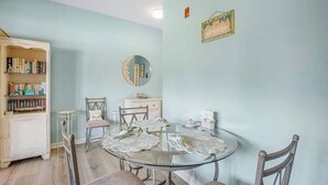 Un comedor con una mesa redonda de vidrio, sillas, una estantería y un espejo colgado en la pared.