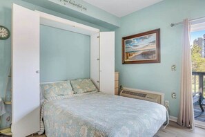 Une chambre à coucher avec un lit, un tableau, un radiateur et une vue sur l’extérieur.