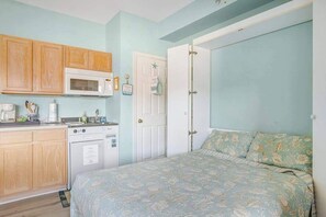 A bedroom with a bed, a door, and a kitchenette with a microwave and stove.