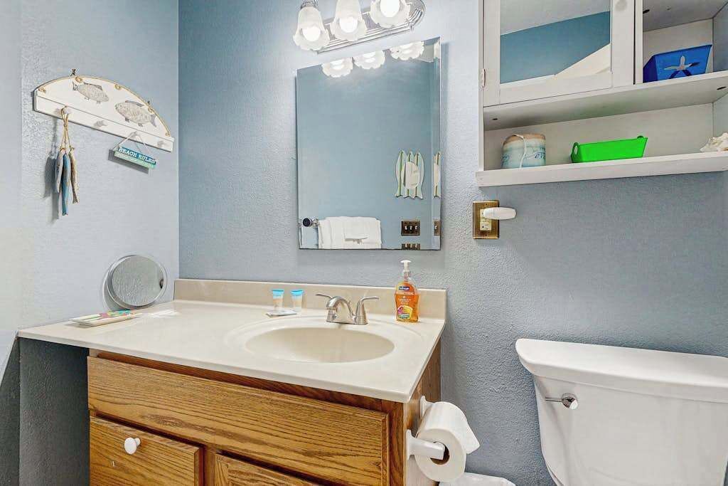 A bathroom with a sink, mirror, toilet, and shelves with toiletries.