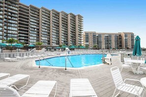 Zona de piscina d'hotel amb gandules, una piscina i edificis alts al fons.