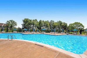 Ein Schwimmbecken mit Liegestühlen und Sonnenschirmen, umgeben von Bäumen.
