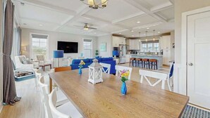 Een ruime woonkamer met een houten eettafel, witte stoelen, een blauwe bank en een keuken op de achtergrond.