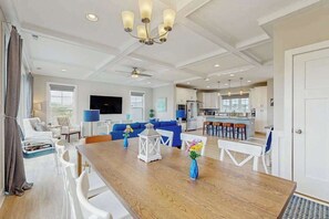 Ein geräumiges Wohnzimmer mit einem Holzespeisetisch, weißen Stühlen, einem blauen Sofa und einer Küche im Hintergrund.