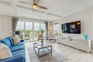 Ein geräumiges Wohnzimmer mit einem großen Fernseher, bequemen Sitzgelegenheiten und einem Balkon mit Blick.