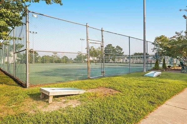 Cancha de tenis con valla, una banca y una mesa pequeña.