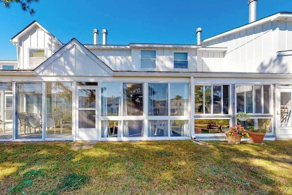 A modern house with a large glass conservatory, white siding, and a chimney.