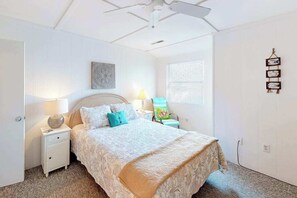 A bedroom with a bed, nightstands, a chair, a ceiling fan, a window with blinds, and wall decorations.