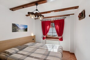 A bedroom with a bed, a window with red curtains, a wooden ceiling, and a wall-mounted light fixture. - Apartment 'Chalet Sever' with Wi-Fi (Livigno)